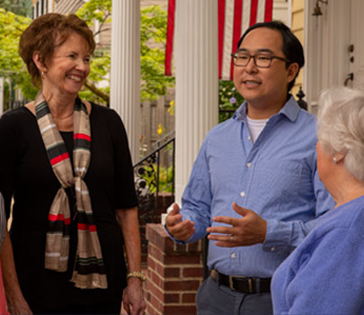 Andy Kim talking with neighbors in front of a house flying an American flag